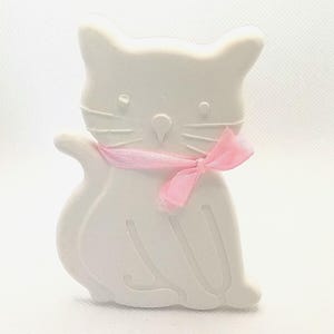 May include: White ceramic cat figurine with a pink ribbon around its neck. The cat is sitting with its tail curled around its legs.