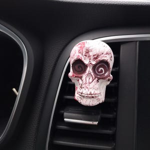 Può includere: Profumatore per auto a forma di teschio bianco con schizzi di vernice rossa e bianca e occhi rossi vorticosi.