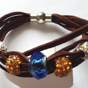May include: A brown leather bracelet with a silver magnetic clasp and five beads. The beads are clear with iridescent accents, orange, and blue.