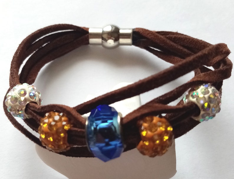 May include: A brown leather bracelet with a silver magnetic clasp and five beads. The beads are clear with iridescent accents, orange, and blue.