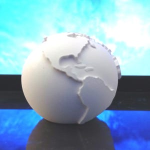 Peut inclure: Un globe terrestre blanc avec une carte en relief des continents. Le globe est posé sur une surface bleue.