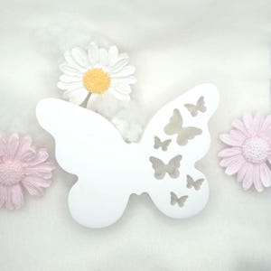 May include: White wooden butterfly wall decoration with cut-out butterfly shapes. The butterfly is surrounded by white and pink flowers.