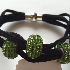 May include: A black suede bracelet with three green crystal beads. The bracelet has a silver magnetic clasp.