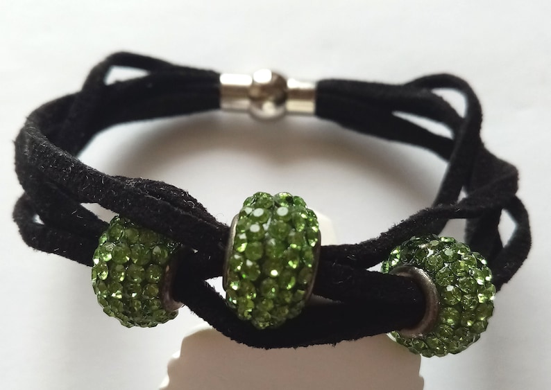 May include: A black suede bracelet with three green crystal beads. The bracelet has a silver magnetic clasp.
