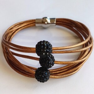 May include: A multi-strand leather bracelet with a magnetic clasp and three black crystal beads.