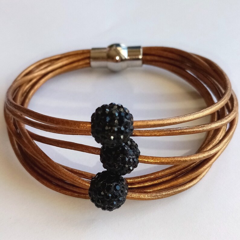 May include: A multi-strand leather bracelet with a magnetic clasp and three black crystal beads.