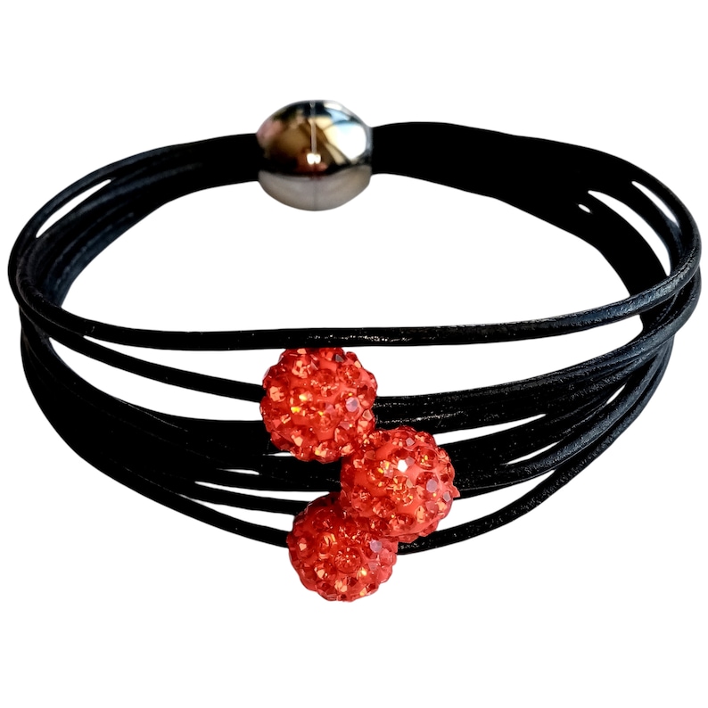 May include: A black leather bracelet with a magnetic clasp and three orange crystal beads.
