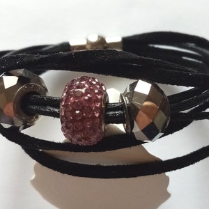 May include: A black suede wrap bracelet with three silver beads. The center bead is pink and sparkly.
