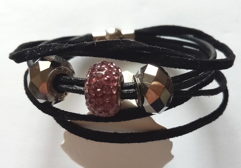 May include: A black suede wrap bracelet with three silver beads. The center bead is pink and sparkly.