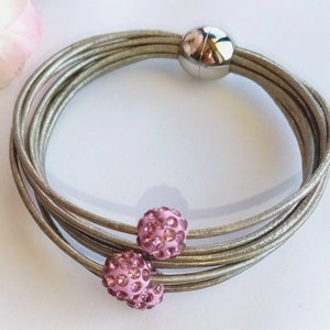 May include: A multi-strand leather bracelet with a magnetic clasp and two pink rhinestone balls.