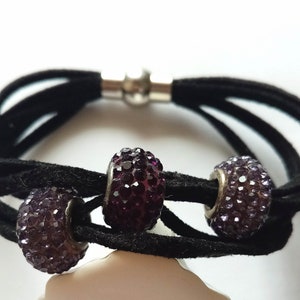 May include: A black suede bracelet with a magnetic clasp and three purple rhinestone beads.