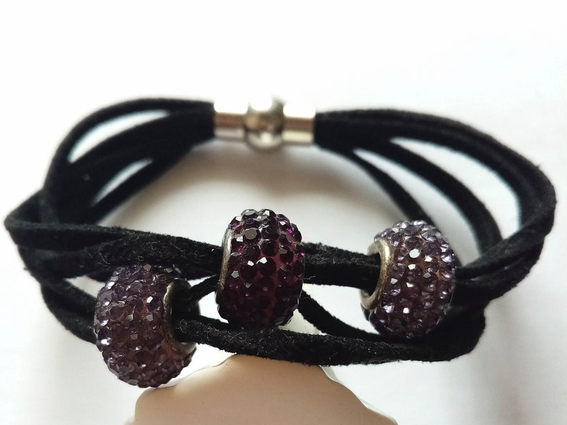 May include: A black suede bracelet with a magnetic clasp and three purple rhinestone beads.