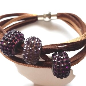 May include: A brown leather bracelet with three purple rhinestone beads. The bracelet has a magnetic clasp.