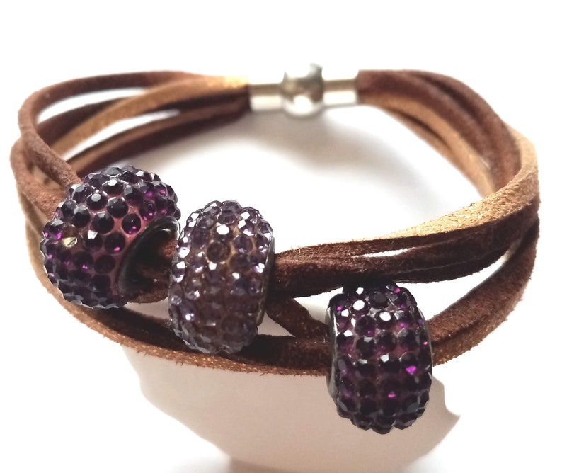 May include: A brown leather bracelet with three purple rhinestone beads. The bracelet has a magnetic clasp.