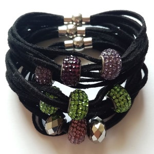 May include: A black suede bracelet with multiple strands and silver magnetic clasps. The bracelet is adorned with colorful crystal beads in shades of purple, green, and pink.