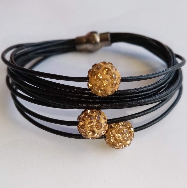 May include: A black leather wrap bracelet with three gold tone rhinestone balls. The bracelet has a magnetic clasp.