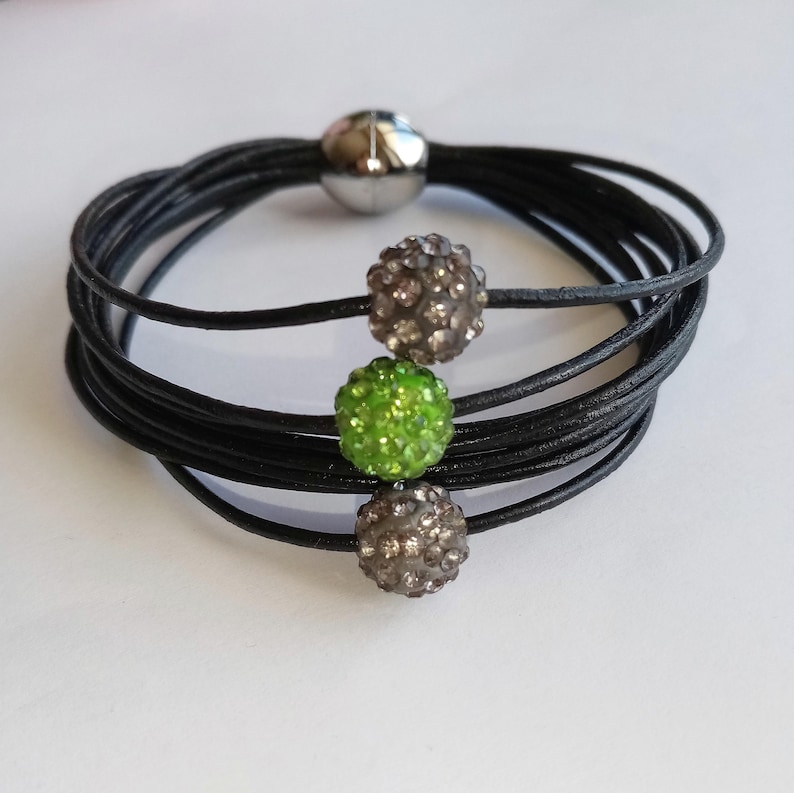 May include: A black leather wrap bracelet with three decorative beads. The beads are silver, green, and silver.