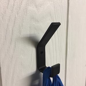 May include: A black metal hook mounted on a white wall with a blue cloth hanging from it.