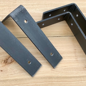 May include: Four black metal shelf brackets with multiple holes for mounting. The brackets are arranged in a staggered pattern on a wooden surface.