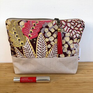 Peut inclure: Une pochette zippée beige avec un imprimé floral dans les tons rouge, jaune et marron. La pochette a un tirette de fermeture éclair à pompon et un fond en lin.