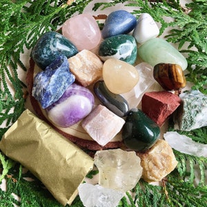 May include: A collection of various colored and textured stones, including amethyst, rose quartz, agate, and jasper. The stones are arranged on a wooden surface with a brown paper wrapping in the foreground.