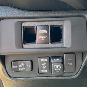 以下が含まれることがあります： 車のダッシュボードのクローズアップで、さまざまなボタンとスイッチがあります。ボタンには、「OFF ON DOOR」、「400W AC 120V 100W」、「REAR PUSH」、「DRL」と表示されています。また、「LED LIGHT BAR」というラベルもあります。