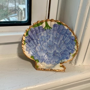 May include: A decorative seashell with a gold trim and a blue hydrangea flower design.
