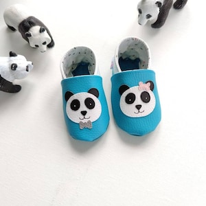 May include: A pair of blue baby shoes with panda bear faces. One panda has a bow tie and the other has a pink bow.