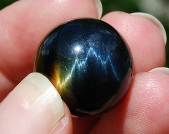 May include: A dark blue and gold sphere with a shimmering, iridescent effect. The sphere is smooth and polished, and it is held in a hand.