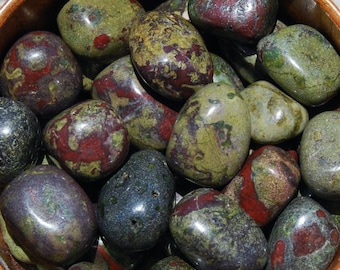 Può includere: Una ciotola piena di pietre di diaspro verde, rosso e nero levigate. Le pietre sono lisce e levigate, con una varietà di motivi e colori.