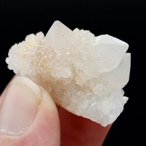 May include: A cluster of small, white quartz crystals with a few yellow inclusions. The crystals are clustered together in a rough, natural formation.