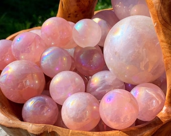 Könnte beinhalten: Eine Holzschale gefüllt mit regenbogenfarbenen rosa Quarzkugeln. Die Schale hat eine natürliche Holzmaserung und einen Griff.
