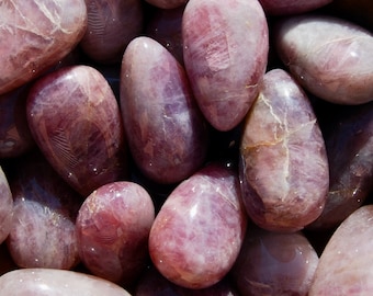 Può includere: Una collezione di pietre di quarzo rosa lucido, in varie tonalità di rosa e viola. Le pietre hanno una forma liscia e arrotondata e un aspetto traslucido, con venature naturali visibili.