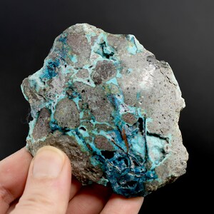 Puede incluir: Una roca gris rugosa con vetas azules y verdes de turquesa. La turquesa está dispersa por toda la roca, creando un patrón único y colorido.