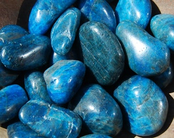 Puede incluir: Una colección de piedras de apatita azul lisas y pulidas. Las piedras son de varios tamaños y formas, con un color azul intenso y un ligero brillo iridiscente.