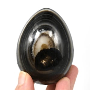 May include: A black and white agate sphere with concentric rings and a dark center. The sphere is polished and smooth.