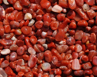 Puede incluir: Una imagen de primer plano de una colección de piedras de cornalina roja. Las piedras son lisas y pulidas, con una variedad de formas y tamaños.