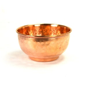 May include: A small, hammered copper bowl with a rounded shape and a slightly flared rim. The bowl has a warm, reddish-brown color and a textured surface. The bowl sits on a small, circular base.