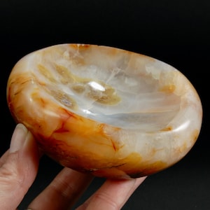 May include: A smooth, polished carnelian bowl with a white interior and orange and red banding. The bowl is carved from a single piece of carnelian.