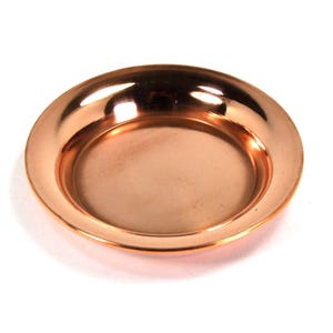 May include: A copper-colored, round plate with a slightly raised rim. The plate has a reflective surface, and the color is a warm, reddish-brown. The plate is likely made of metal and is sitting on a white surface.