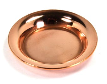 May include: A copper-colored, round plate with a slightly raised rim. The plate has a reflective surface, and the color is a warm, reddish-brown. The plate is likely made of metal and is sitting on a white surface.