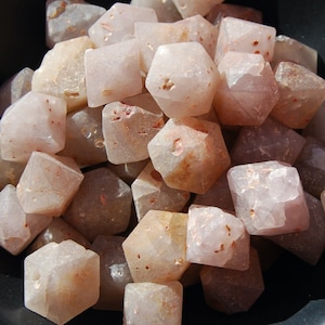 Può includere: Una collezione di cristalli di quarzo sfaccettati di colore rosa e marrone. I cristalli sono di varie dimensioni e forme, e sono tutti levigati e lucidati.