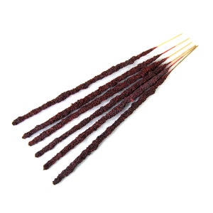 Puede incluir: Un paquete de seis varillas de incienso con una superficie texturizada de color rojo oscuro y una punta de madera fina de color marrón claro.