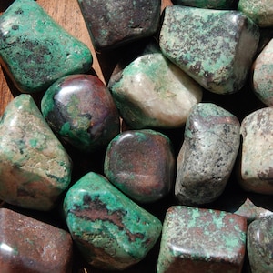 May include: A collection of tumbled green and brown stones with a mottled, marbled appearance. The stones are smooth and polished, with a variety of shapes and sizes.