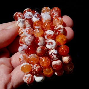 May include: A strand of round, orange agate beads with white and brown inclusions. The beads are approximately 8mm in diameter and have a polished finish.