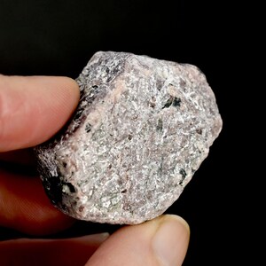 May include: A rough, gray and pink ruby crystal with a slightly reddish hue. The crystal has a natural, unpolished look.