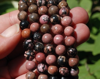 May include: A strand of pink and black gemstone beads. The beads are round and have a mottled appearance.