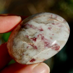 May include: A white and red tumbled stone with a smooth, oval shape. The stone has a marbled appearance with red and white streaks.