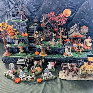 May include: A Halloween village display featuring miniature haunted houses, trees with orange leaves, pumpkins, and figures. Includes a horse-drawn carriage, a well, and a sign that reads "Jack's Pumpkin Farm".