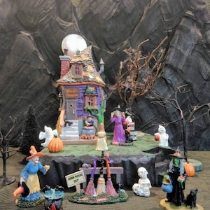 May include: A miniature Halloween village scene with a witch's house, a witch, a cauldron, a pumpkin, a ghost, and a sign that says "Broom Parking Only".